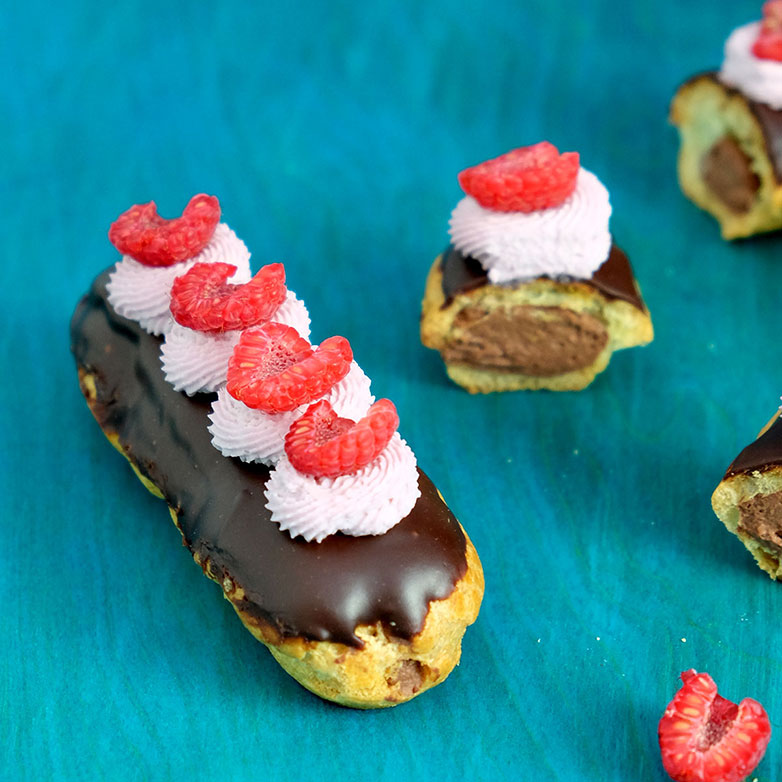 Chocolate topped eclairs with chocolate filling, with raspberry cream topping and sliced raspberries. 